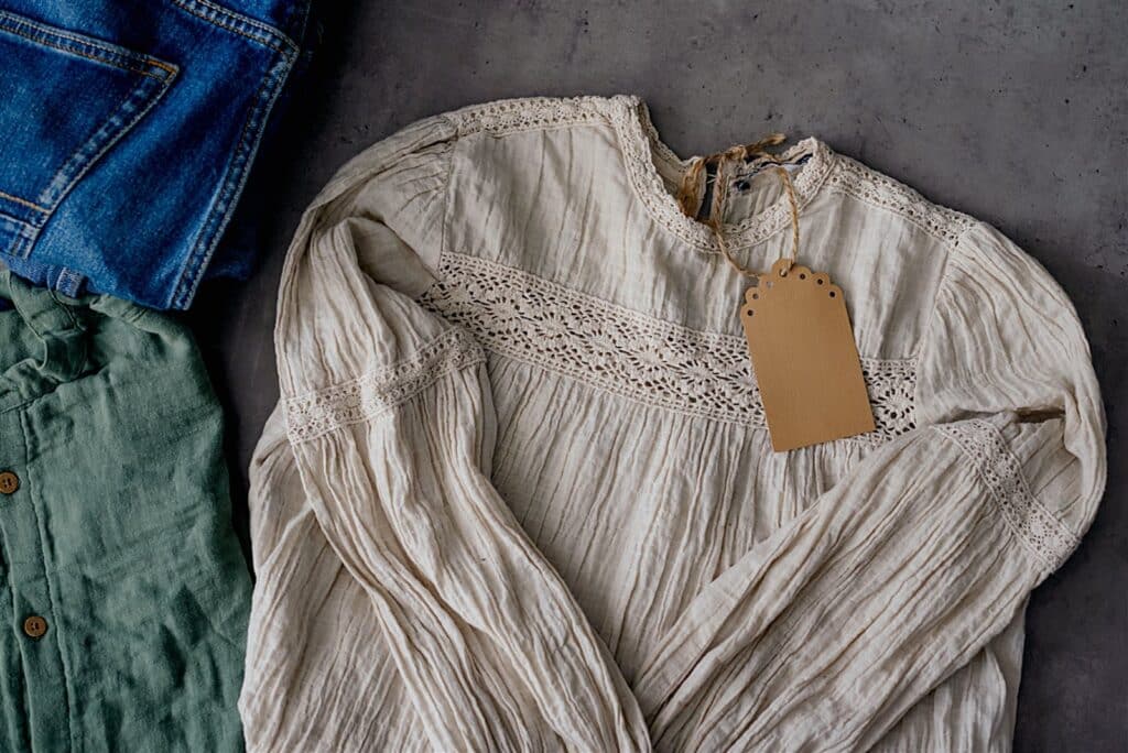 Cream lace-trimmed blouse beside folded blue denim and green clothing.